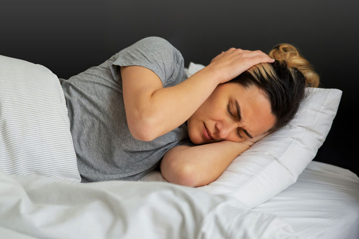 Schlafstörungen durch Lärm, Frau im Bett hält sich aufgrund von Lärm die Ohren zu.